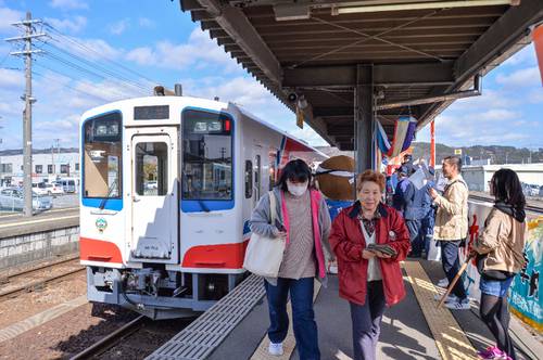 関係者らに出迎えられ、笑顔で久慈駅に降りる乗客＝１４日午前９時半ごろ
