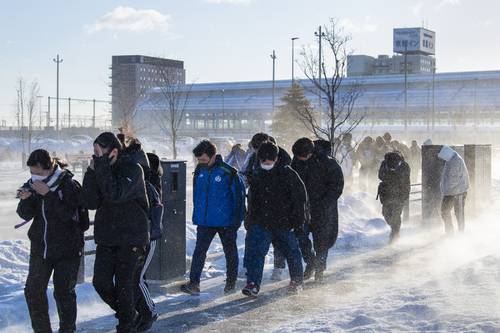 強風が積もった雪を舞い上げる中、寒さをこらえて登校する学生＝３０日午前８時ごろ、八戸駅前